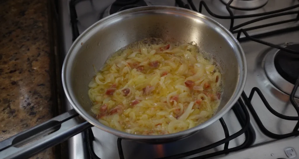 bacon com manteiga e cebola em uma frigideira de inox