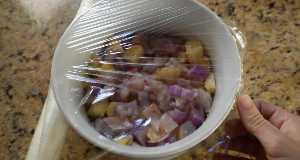 Testei a receita de ceviche com abacaxi do Panelinha plástico filme na tigela com ceviche com abacaxi pronto para ir para a geladeira